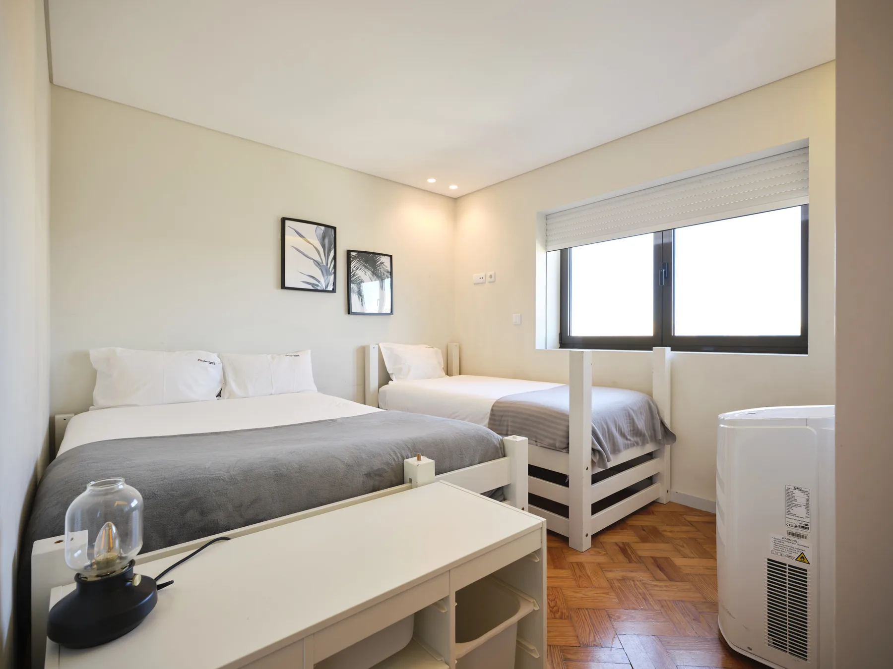 A bright bedroom with two beds, framed artwork, and a large window.