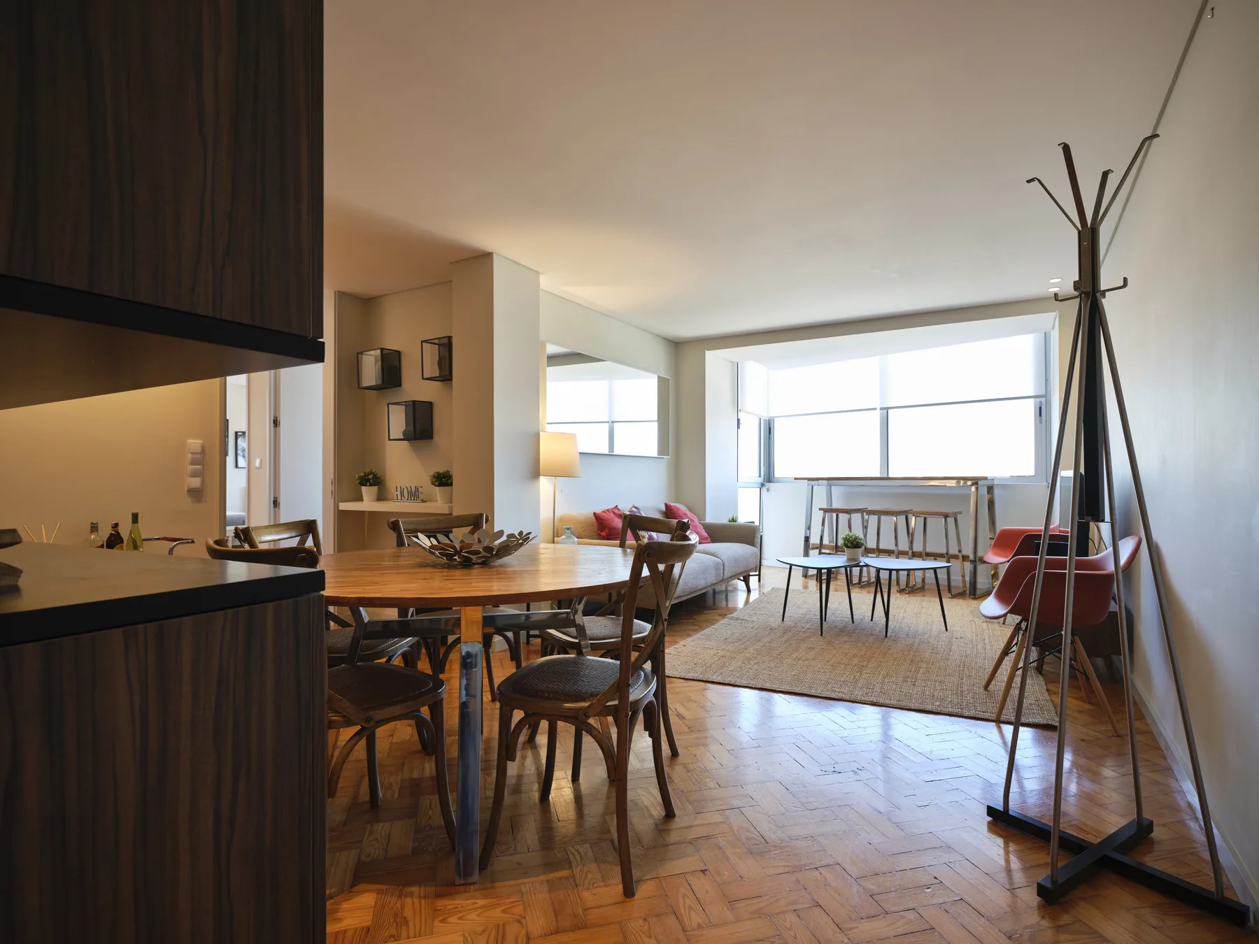 A bright apartment living and dining area with seating beside large windows.