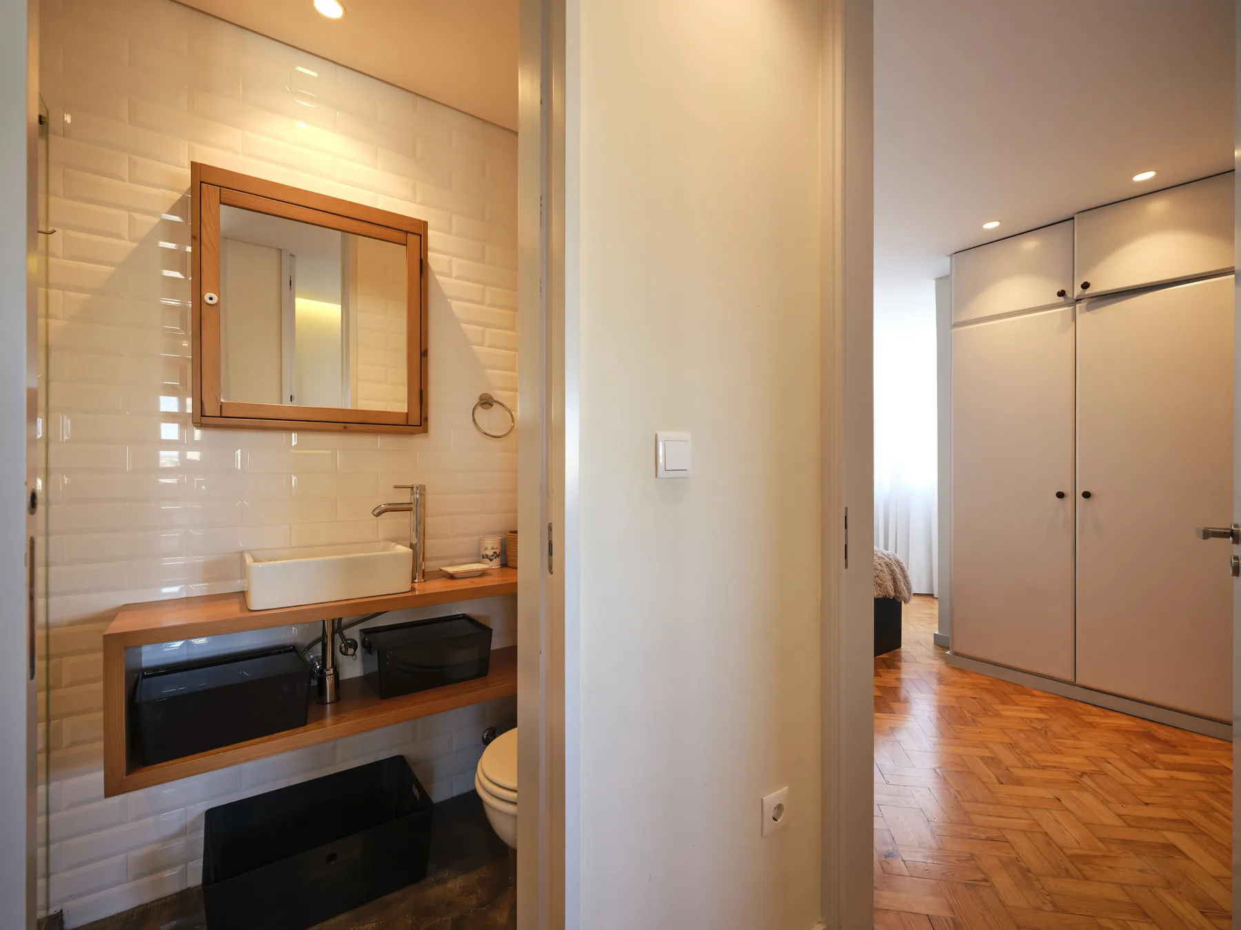 A bathroom vanity with a mirror opens onto a bedroom with a wardrobe.