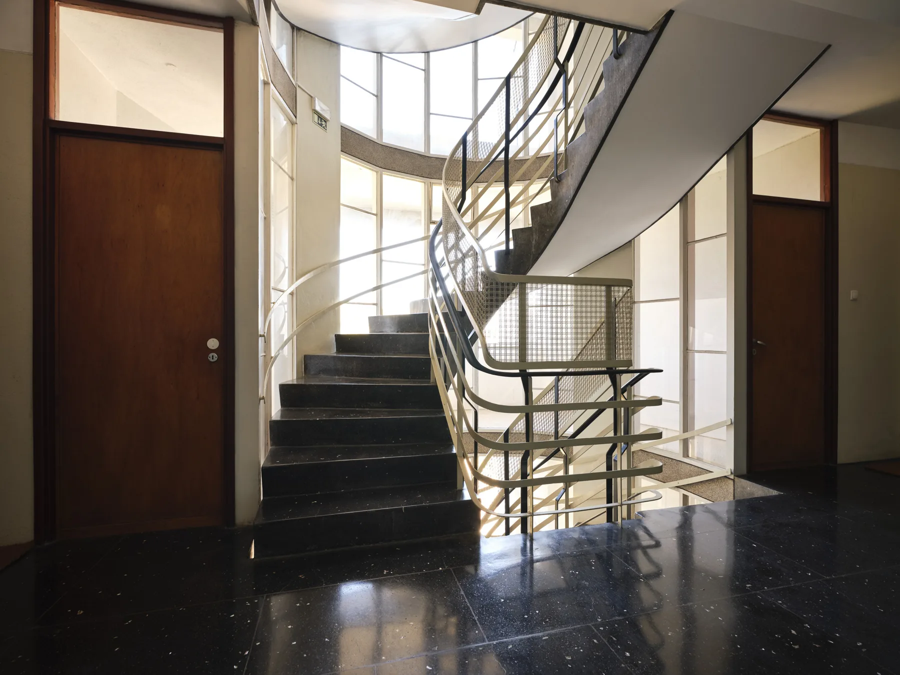 A bright interior stairwell with curved steps and large windows.