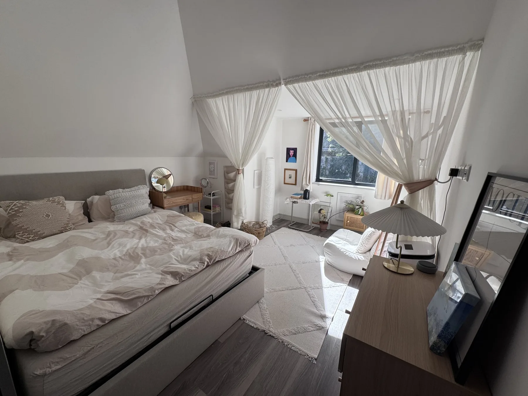 A bright bedroom with a bed, sheer curtains, and a window.