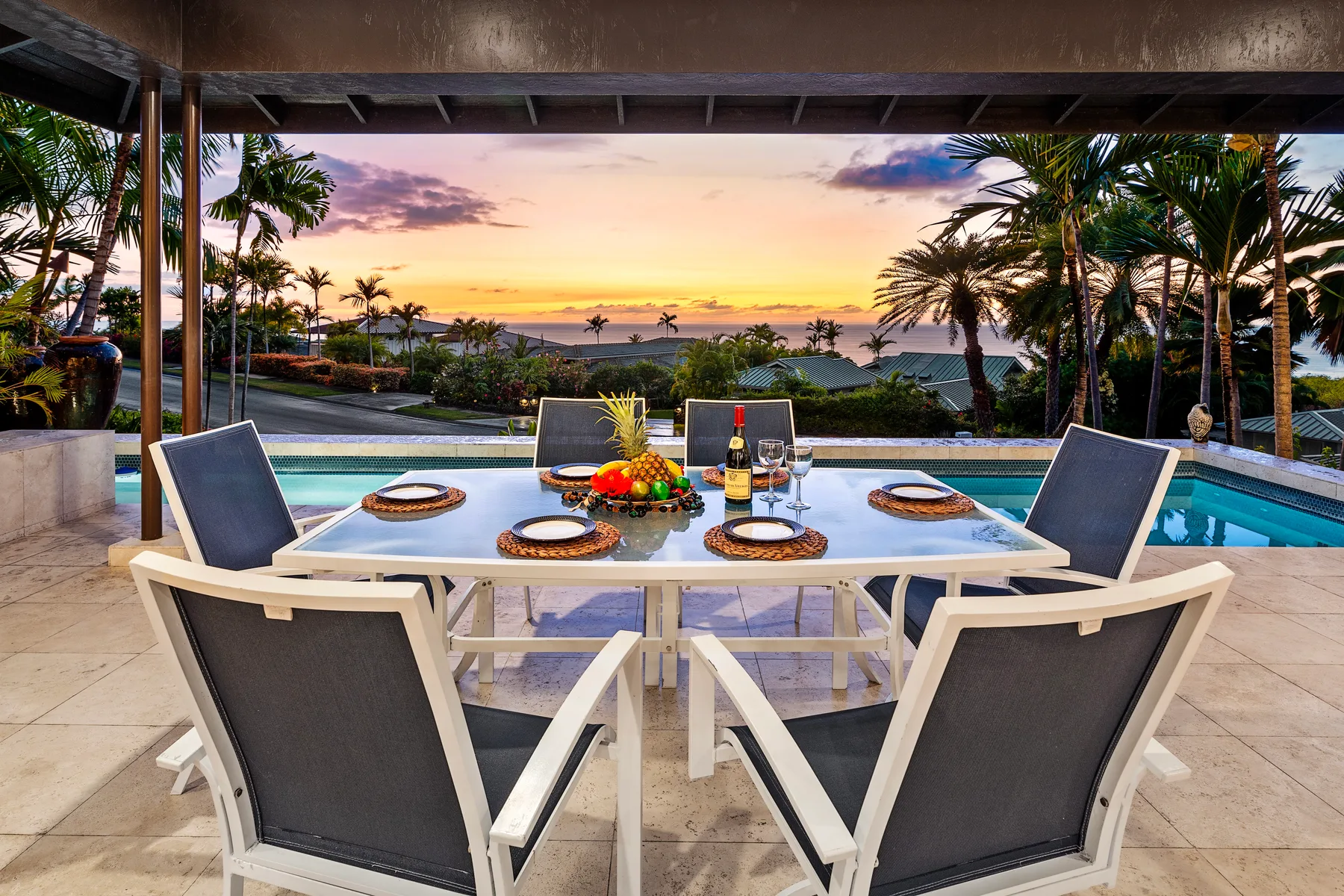 Un comedor en una terraza da a una piscina y al océano al atardecer.