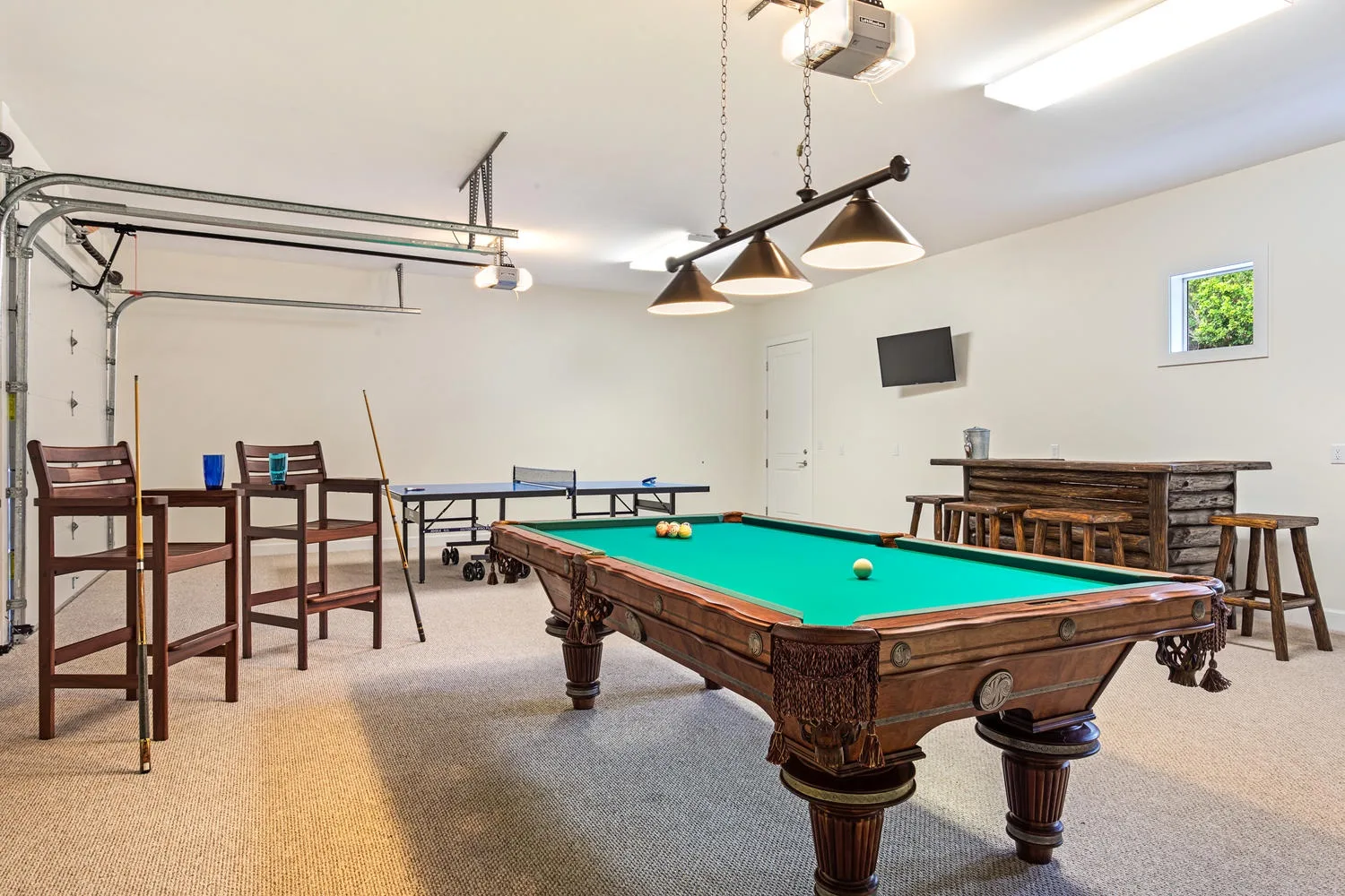 Una sala de recreación tiene una mesa de billar con paño verde y varios taburetes.