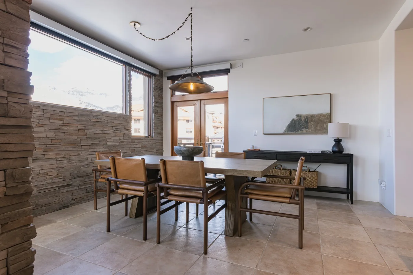 Un comedor con una mesa de madera y sillas junto a grandes ventanas.