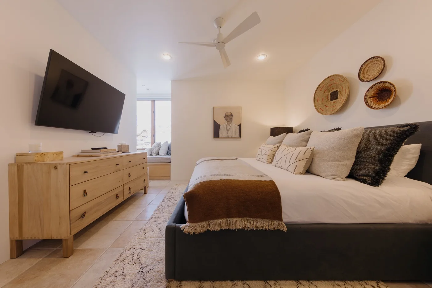 Un dormitorio con una cama bien arreglada, un televisor montado en la pared y adornos tejidos.