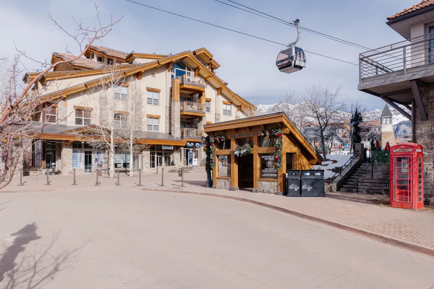 Una plaza peatonal con edificios de estilo chalet, un pequeño quiosco y una góndola aérea.
