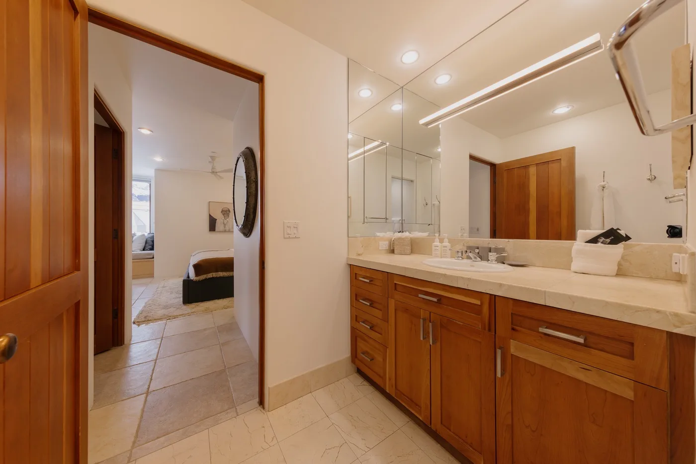 Un lavabo de baño con un espejo amplio y una puerta hacia una habitación contigua.