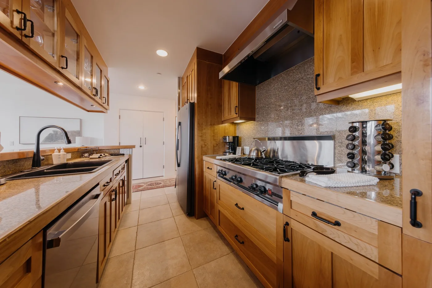 A kitchen with wooden cabinets, stone countertops, and a cooktop.