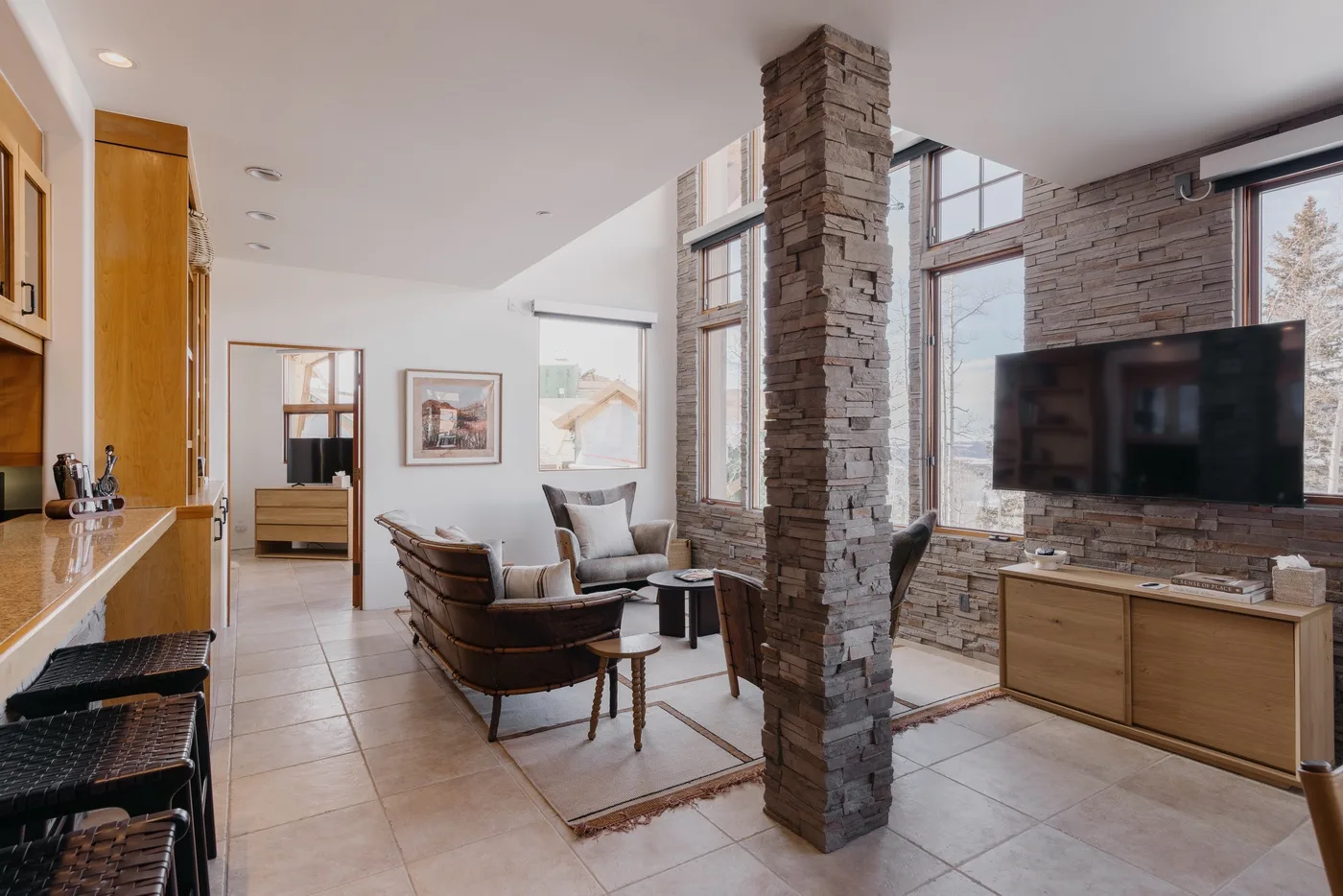 A bright living room has seating arranged beside a television and tall windows.