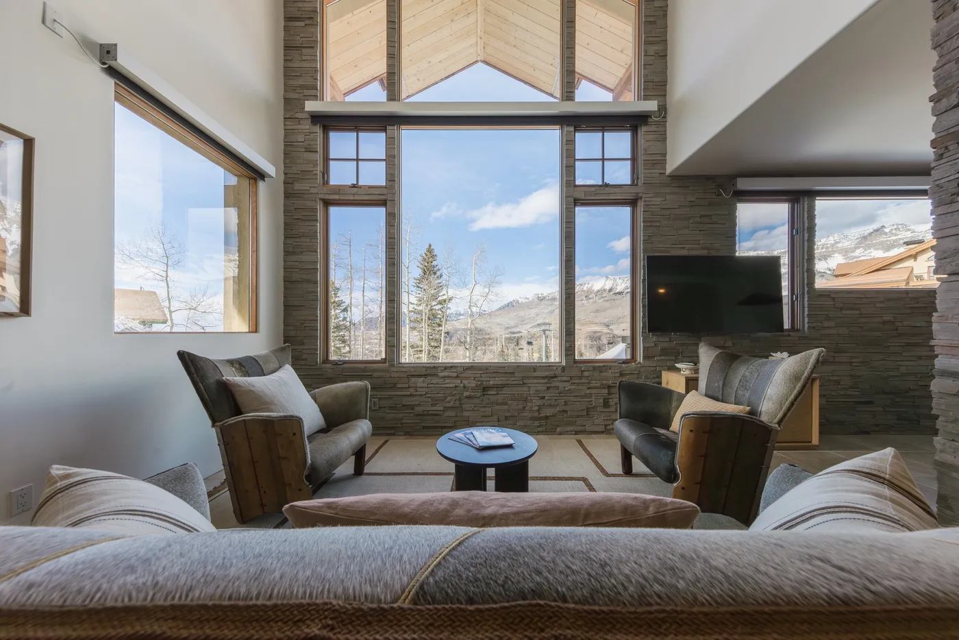 Una amplia sala de estar tiene asientos alrededor de una mesa pequeña junto a grandes ventanas.