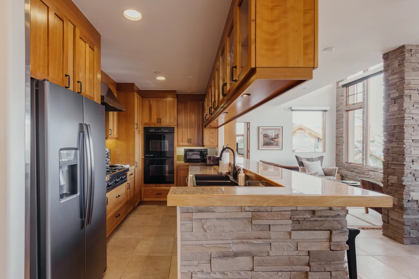 Cocina con gabinetes de madera e isla revestida de piedra junto a un comedor con ventanas.