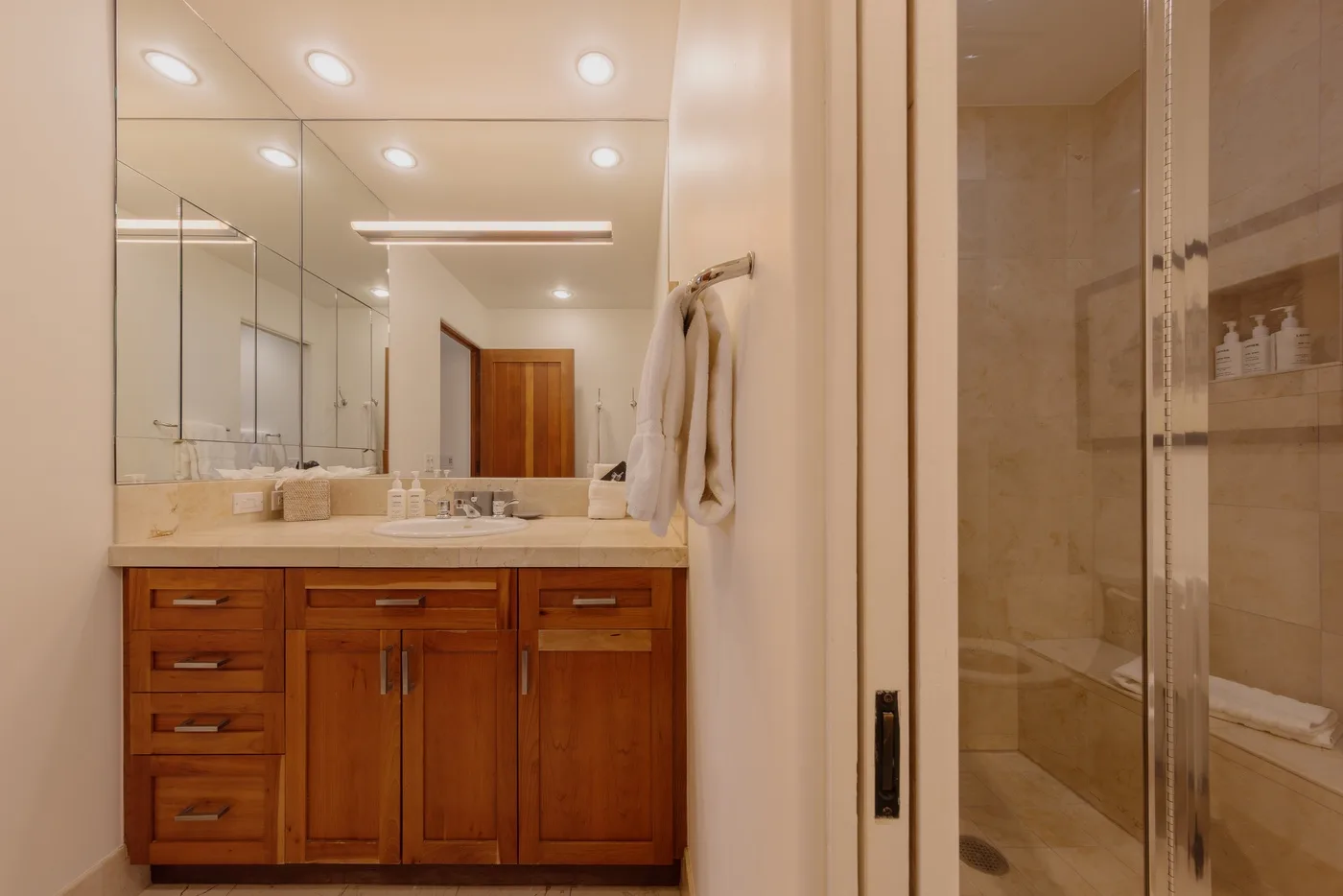 Un lavabo de baño con un espejo amplio está junto a una ducha con mampara de vidrio.