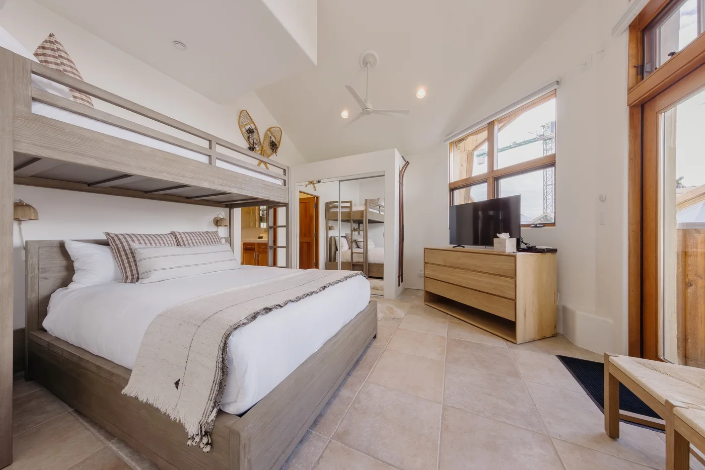 Un dormitorio luminoso con una cama alta, ropa de cama arreglada y un televisor.