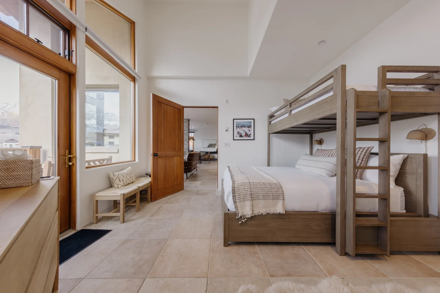 Un dormitorio luminoso con una litera de madera y grandes ventanas.