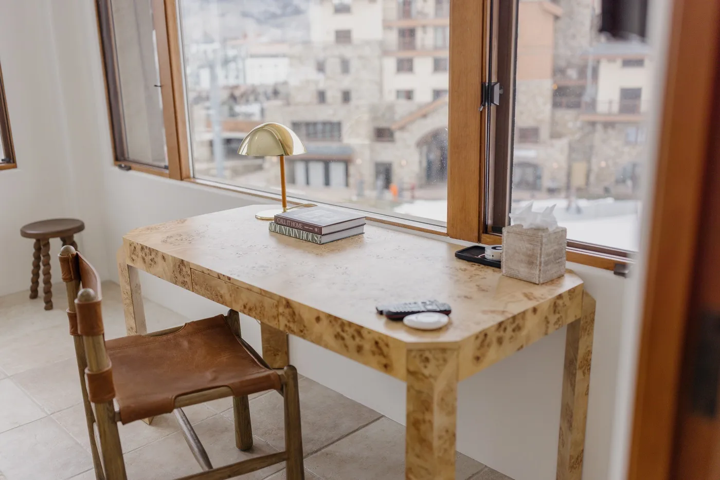 Una mesa y asientos están junto a grandes ventanas con vista a edificios cercanos.