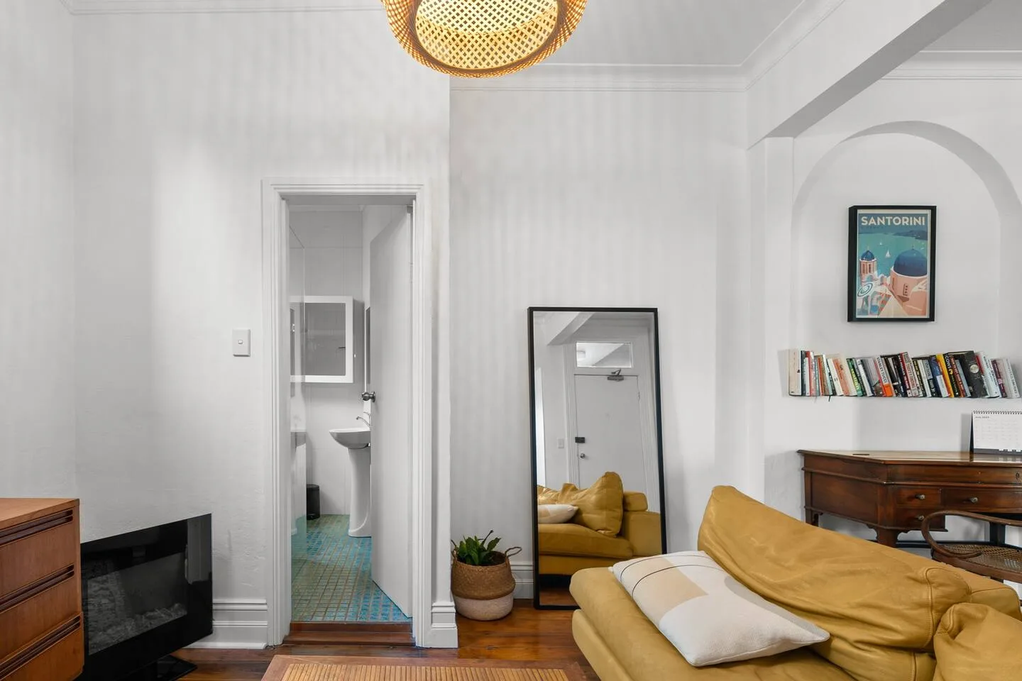 Una sala luminosa con asientos, un espejo de cuerpo entero y una pequeña estantería.