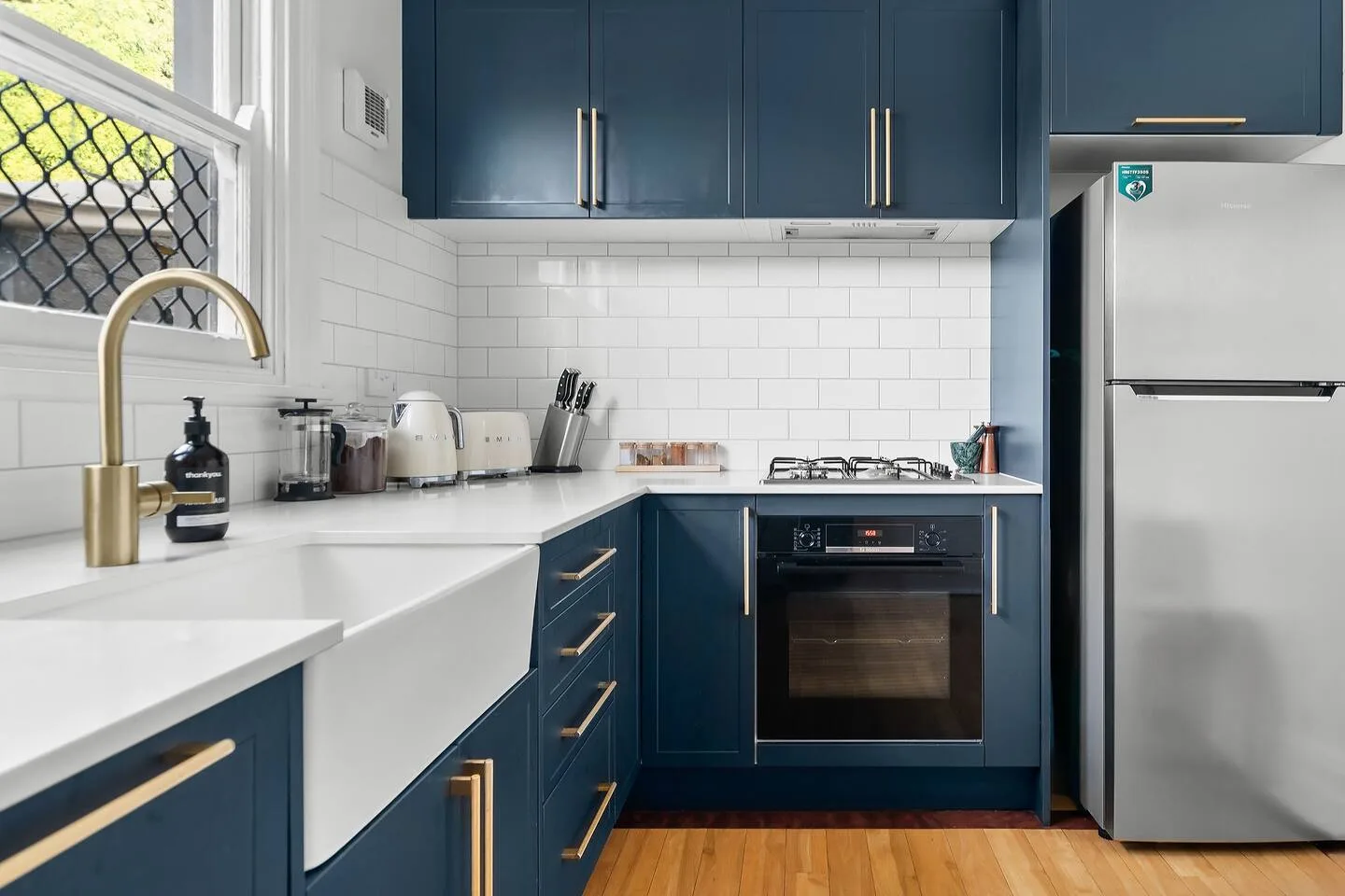 Elegantes armarios azules, azulejos tipo metro, electrodomésticos de alta gama y grifería dorada cepillada adornan la cocina bien equipada.
