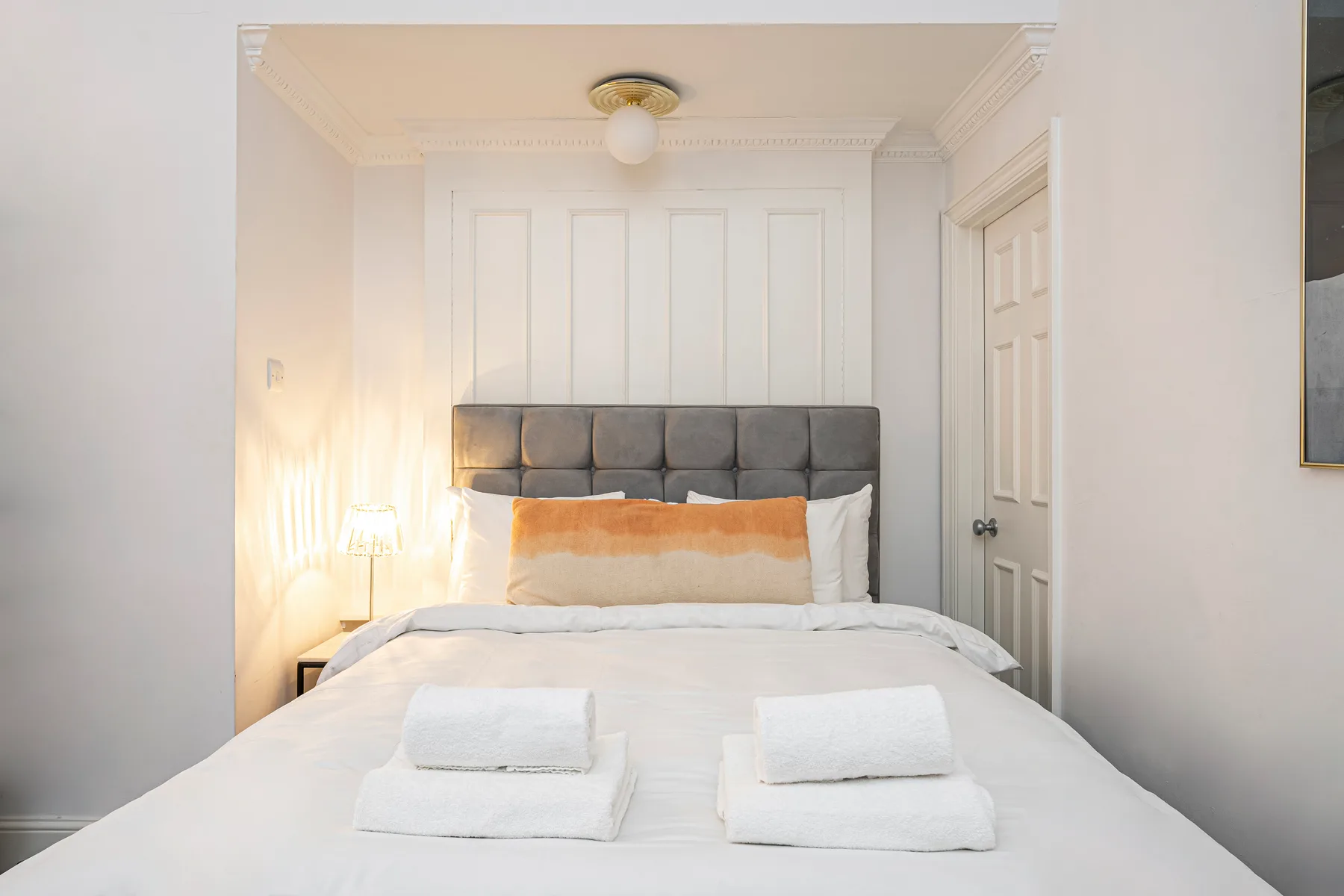 A bedroom with a neatly made bed and a gray upholstered headboard.