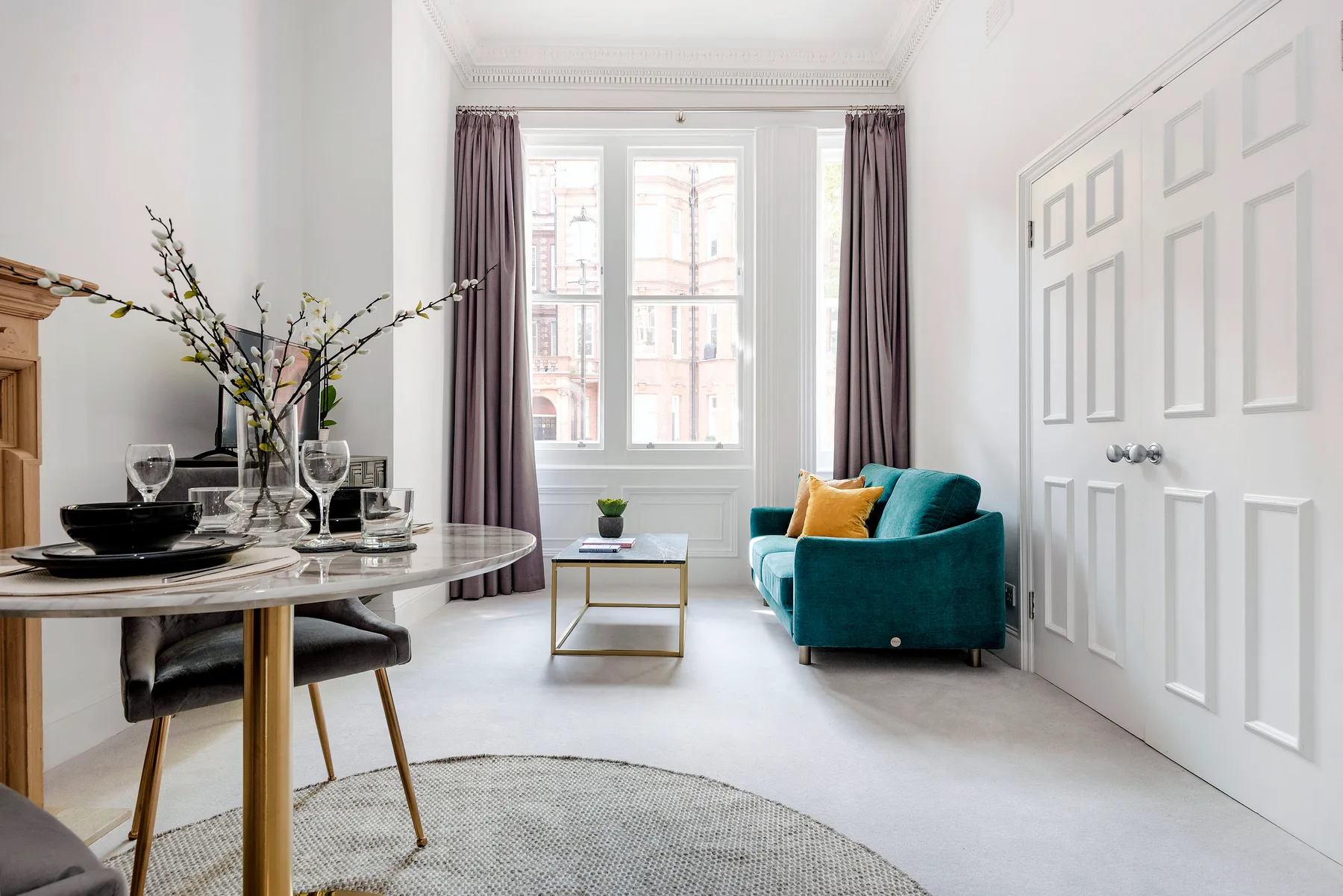 A bright living and dining area with teal seating beside a large window.
