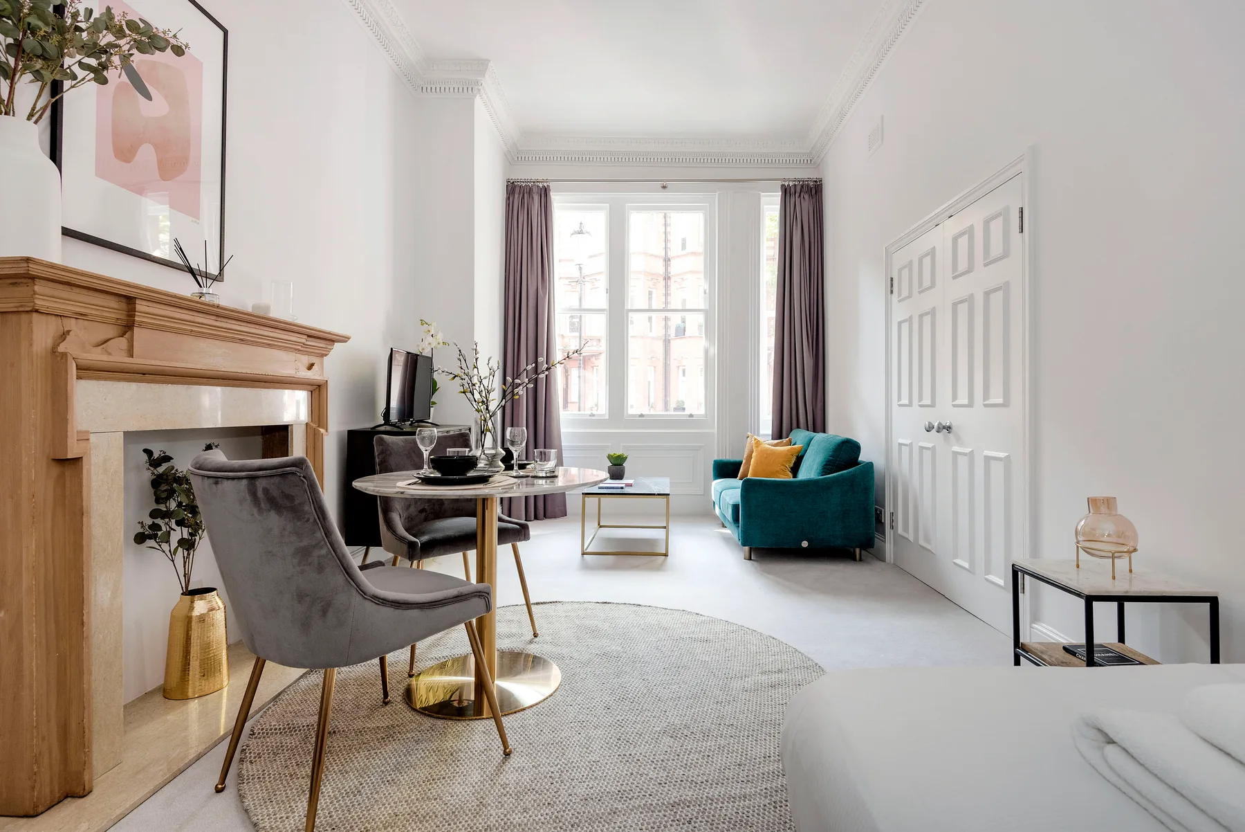 A bright sitting room with a fireplace, round table, and teal seating.