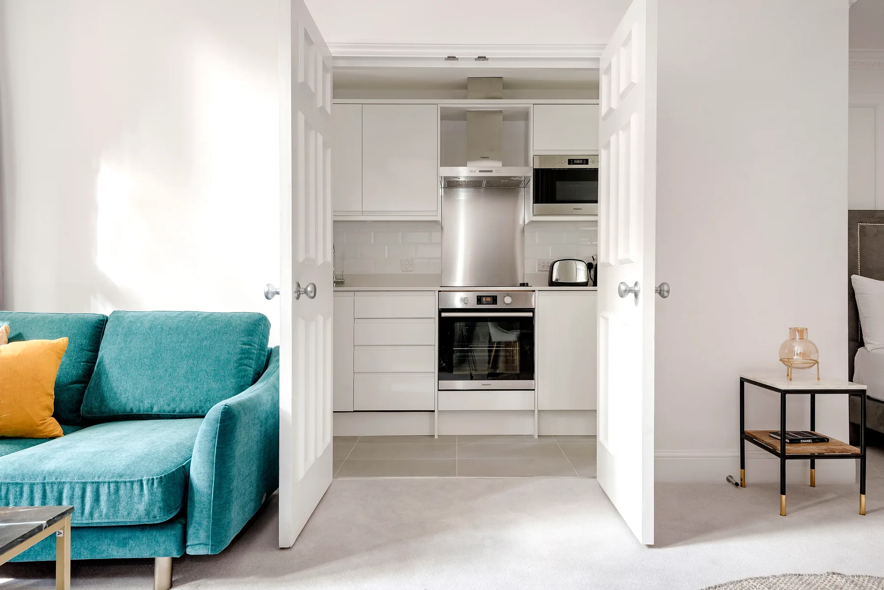 An open-plan living area with teal seating and a compact white kitchen.