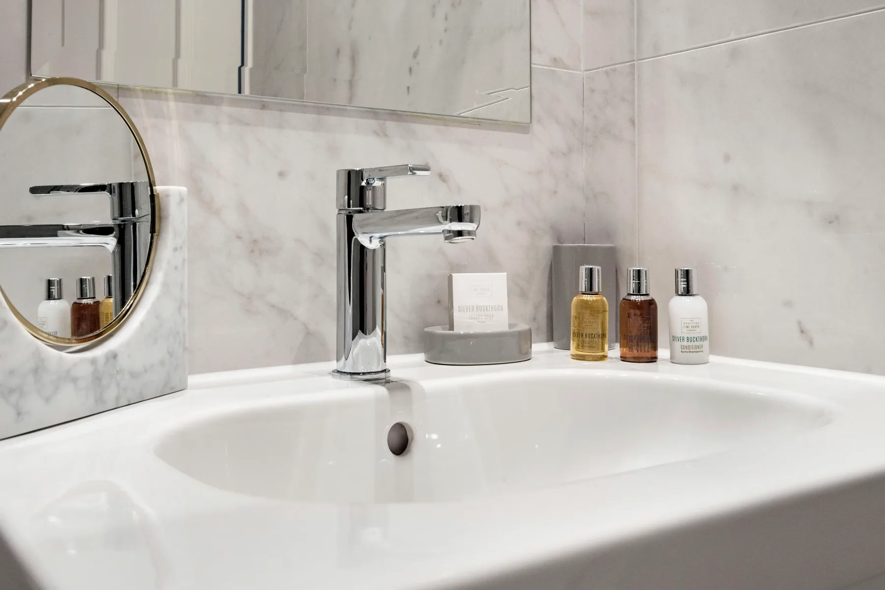 A bathroom sink sits beneath a mirror, with toiletries arranged beside the faucet.