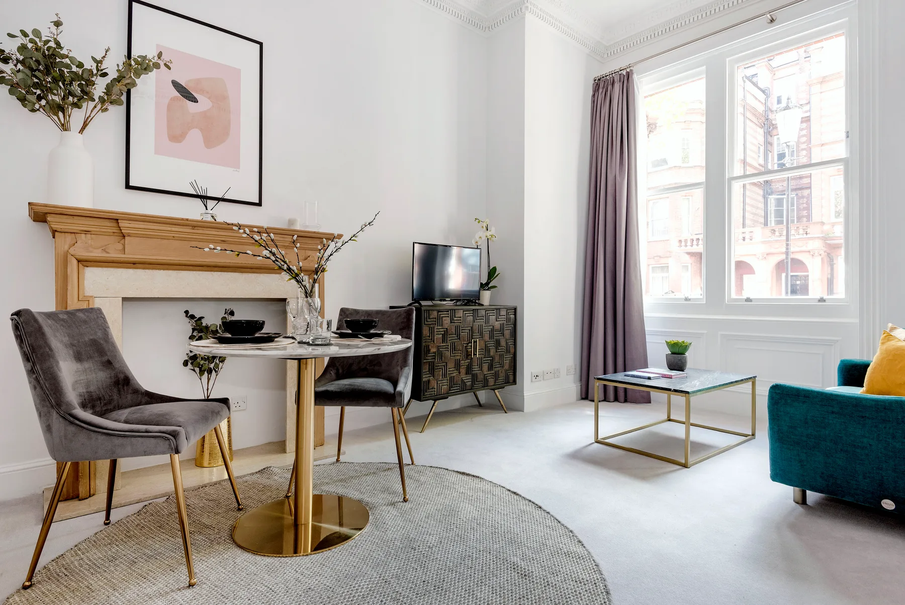 A bright living room with a dining table, television, and seating beside large windows.