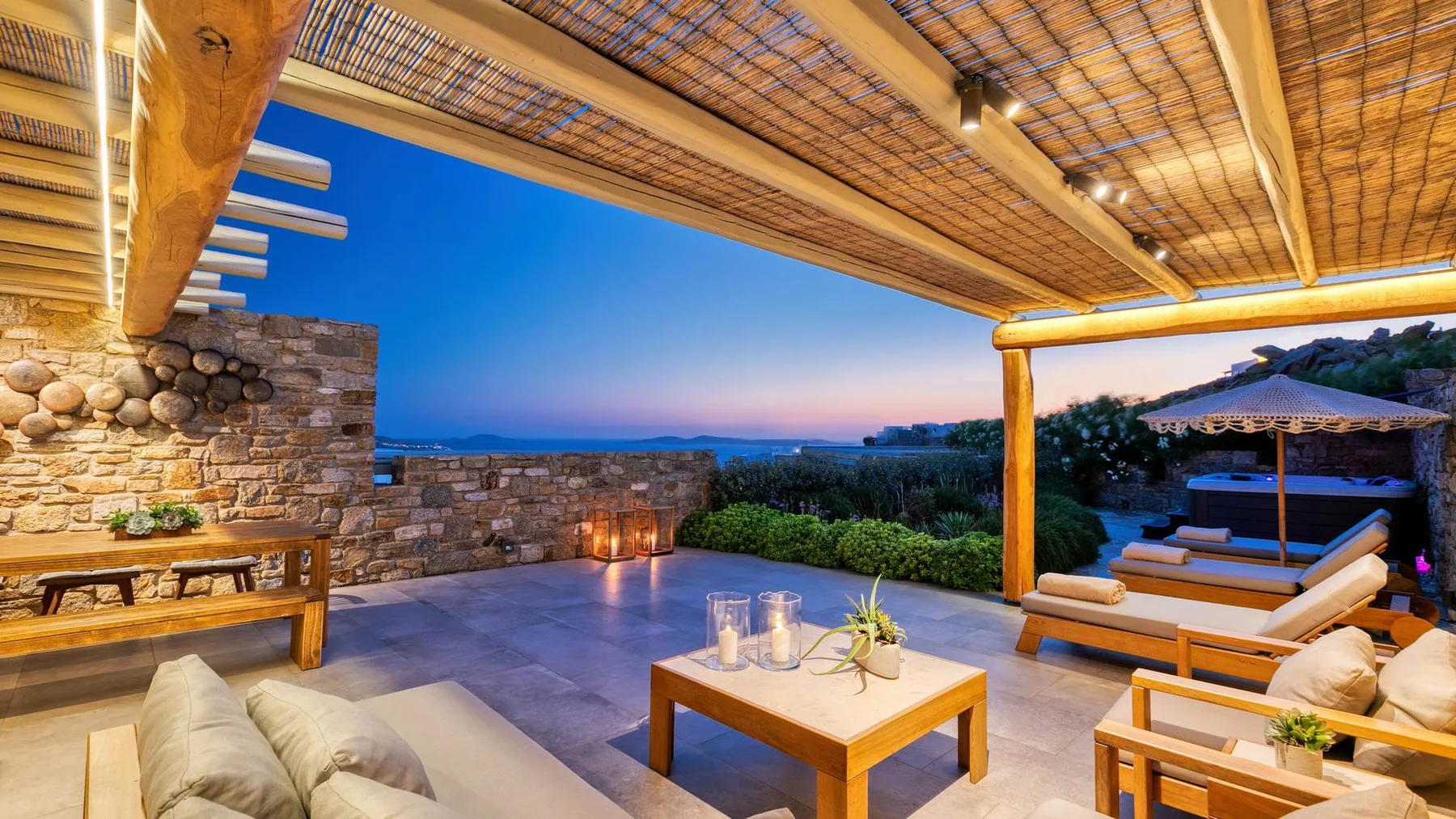 An outdoor lounge area with cushioned seating, a low table, and a sea view.