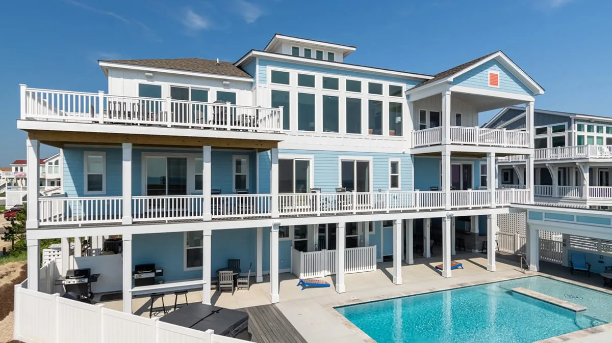 A large blue multi-story building with white balconies stands beside a swimming pool.