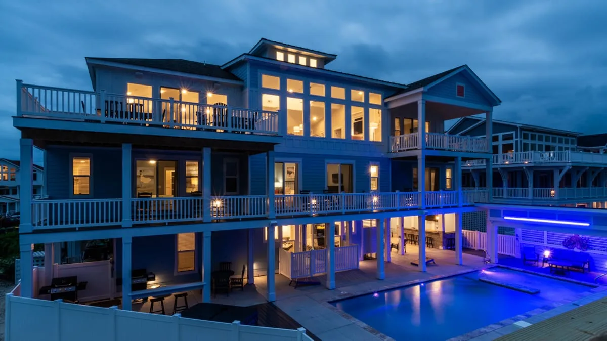 A large house with balconies and a lit swimming pool at dusk.