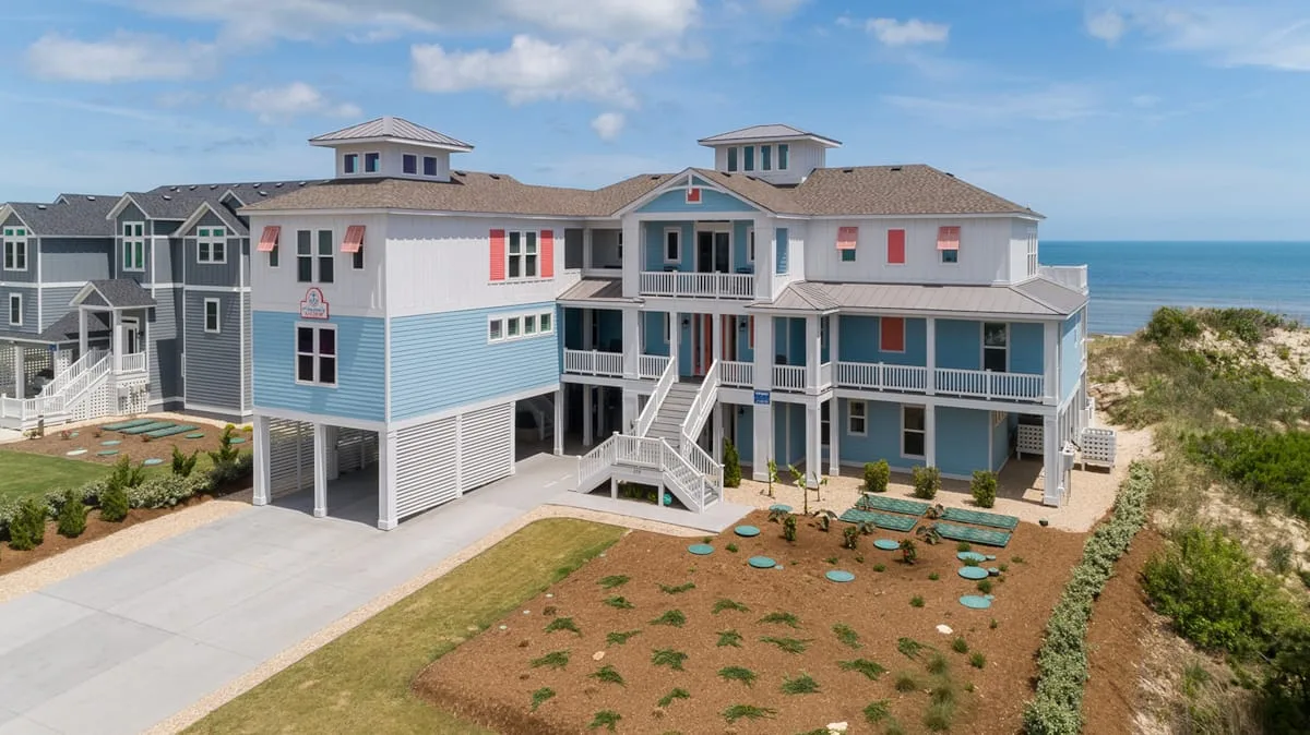 A large coastal house with blue siding, white balconies, and landscaped grounds.