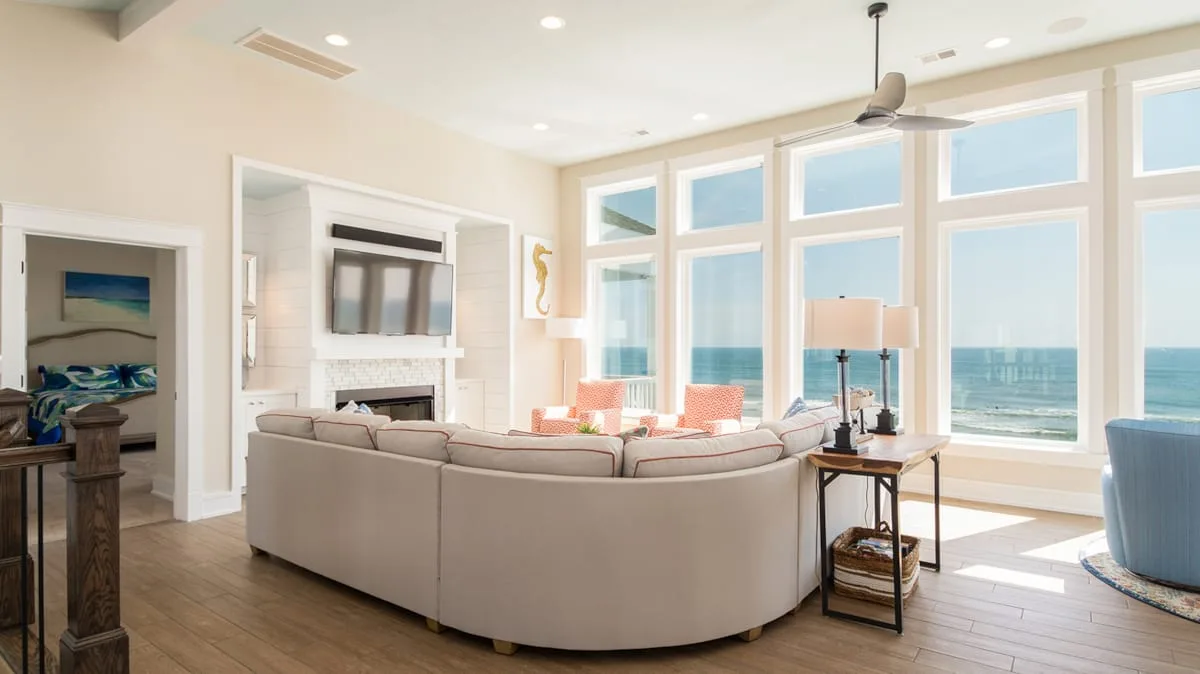 A bright living room with seating beside large windows overlooking the ocean.