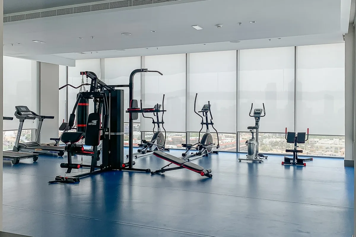 A gym with exercise machines arranged beside large windows.