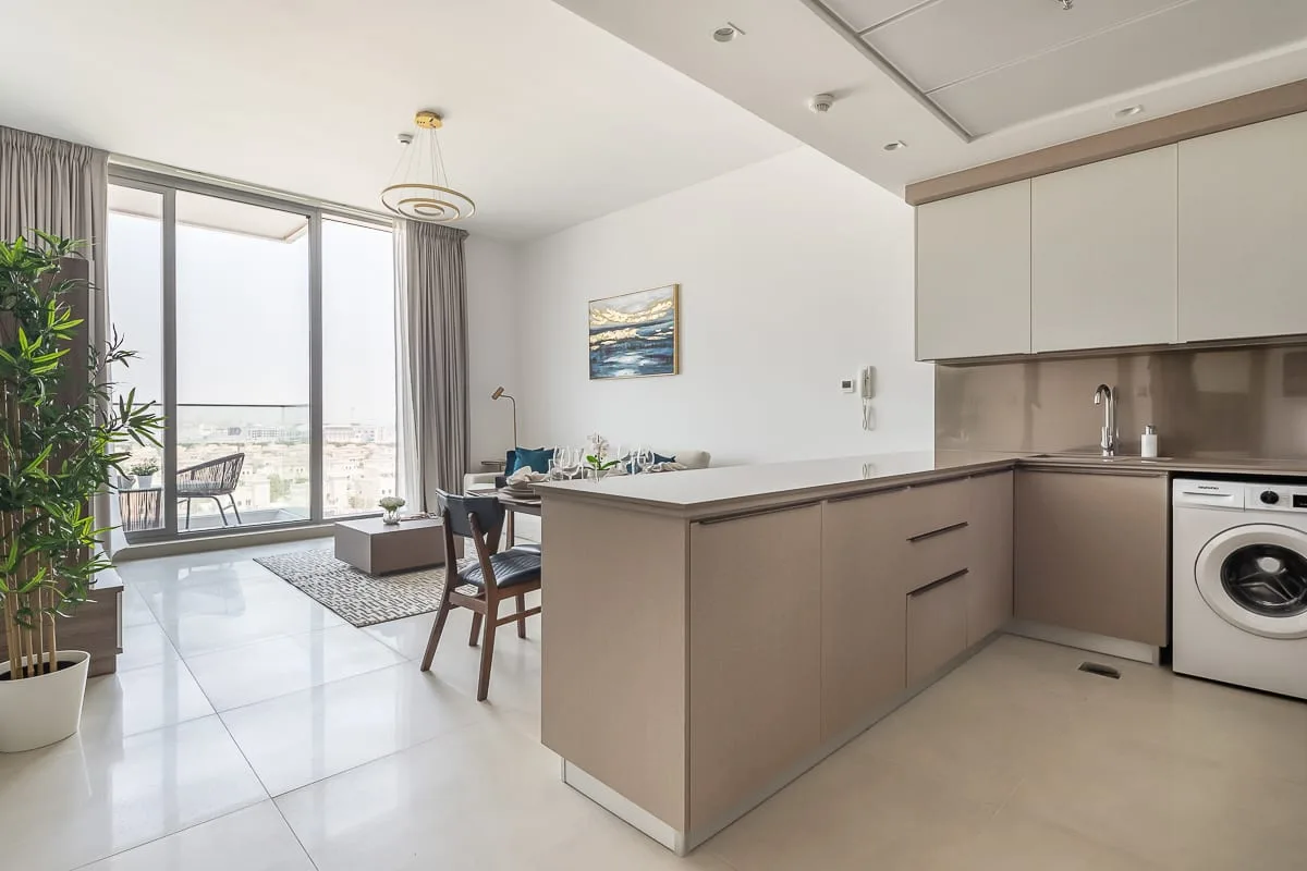An open-plan kitchen and dining area beside large windows and a small living space.