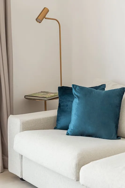 A white seating area with teal cushions and a slim floor lamp.