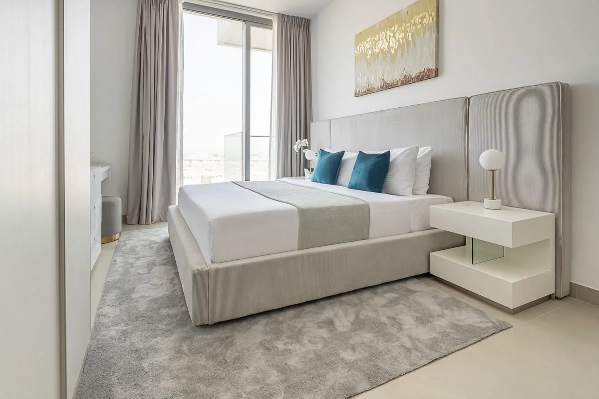 A bright bedroom with a neatly made bed and a large window.