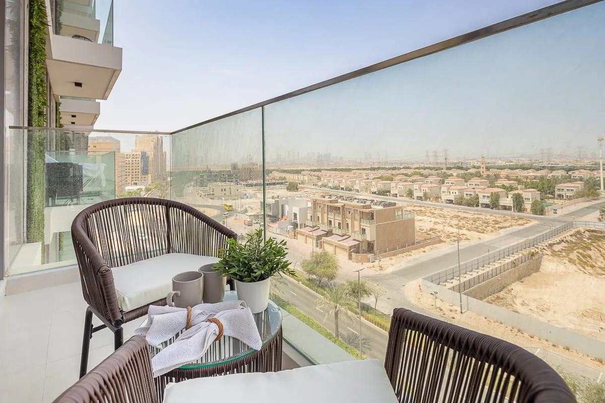 A balcony seating area overlooks a neighborhood through a glass railing.