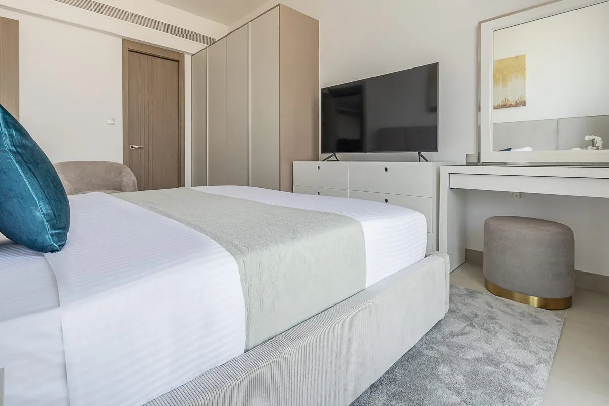 A bedroom with a neatly made bed, television, and dressing table.