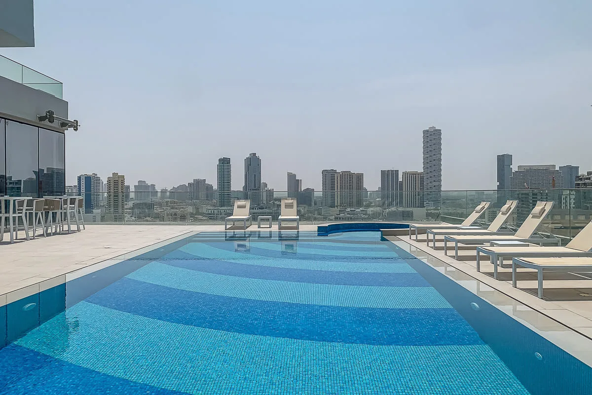 A rooftop swimming pool is surrounded by lounge seating and city views.