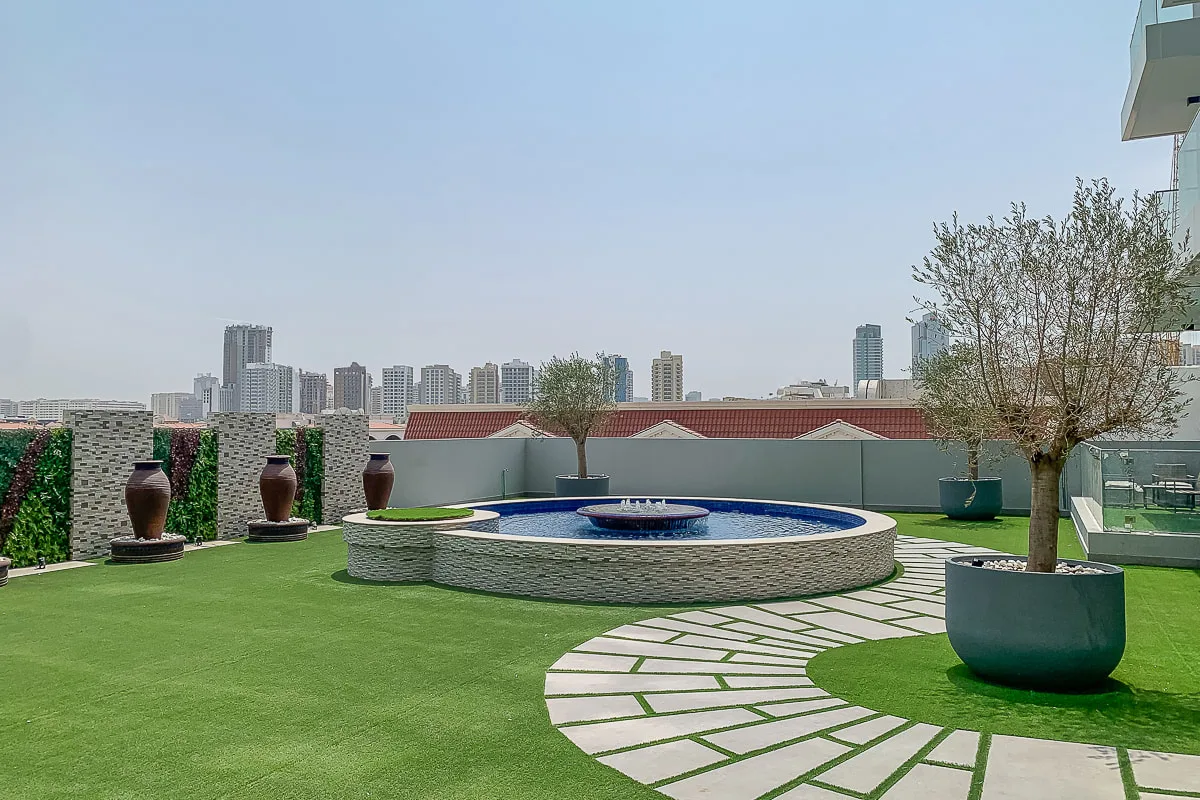 A rooftop garden with a circular fountain and paved walkway.