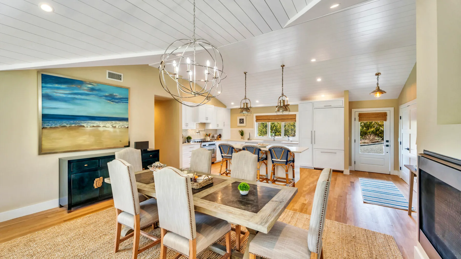 An open dining and kitchen area with a long table and pendant lights.