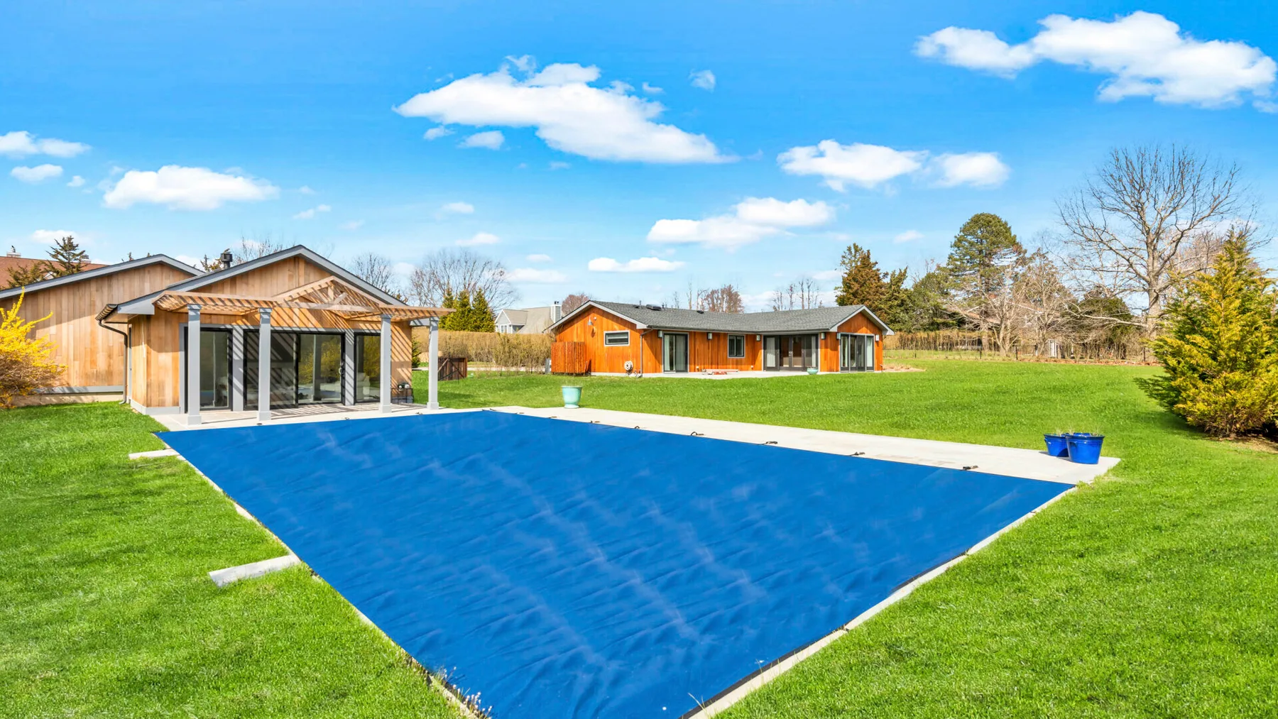 A covered swimming pool sits beside a lawn and low buildings.