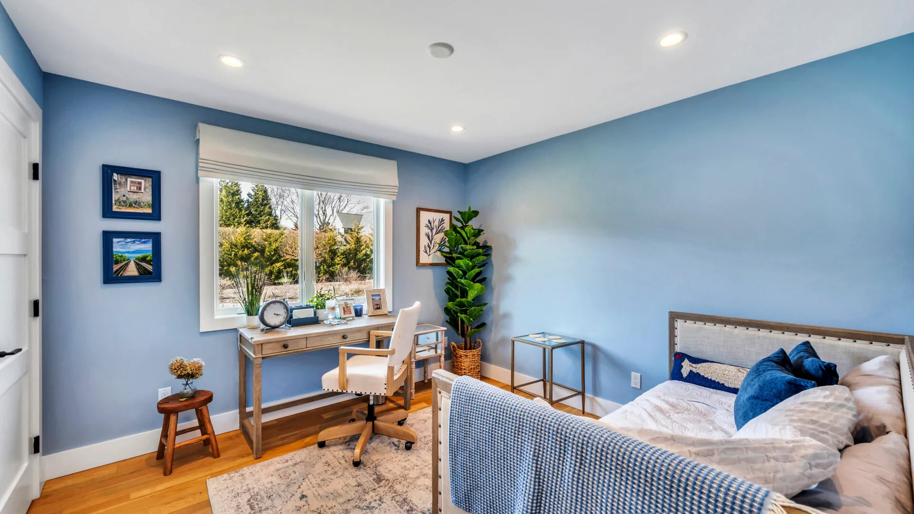 A bright bedroom with a desk beside the window and a bed.