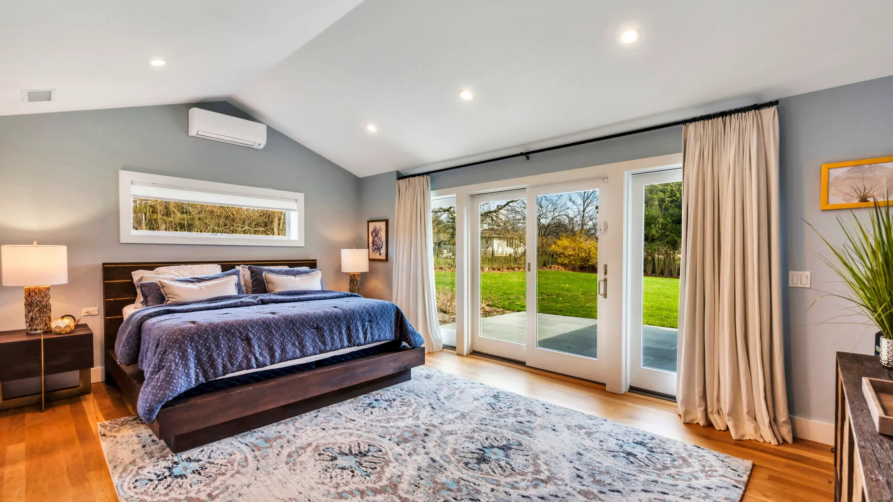 A bedroom with a large bed, a patterned rug, and glass doors opening onto a garden.