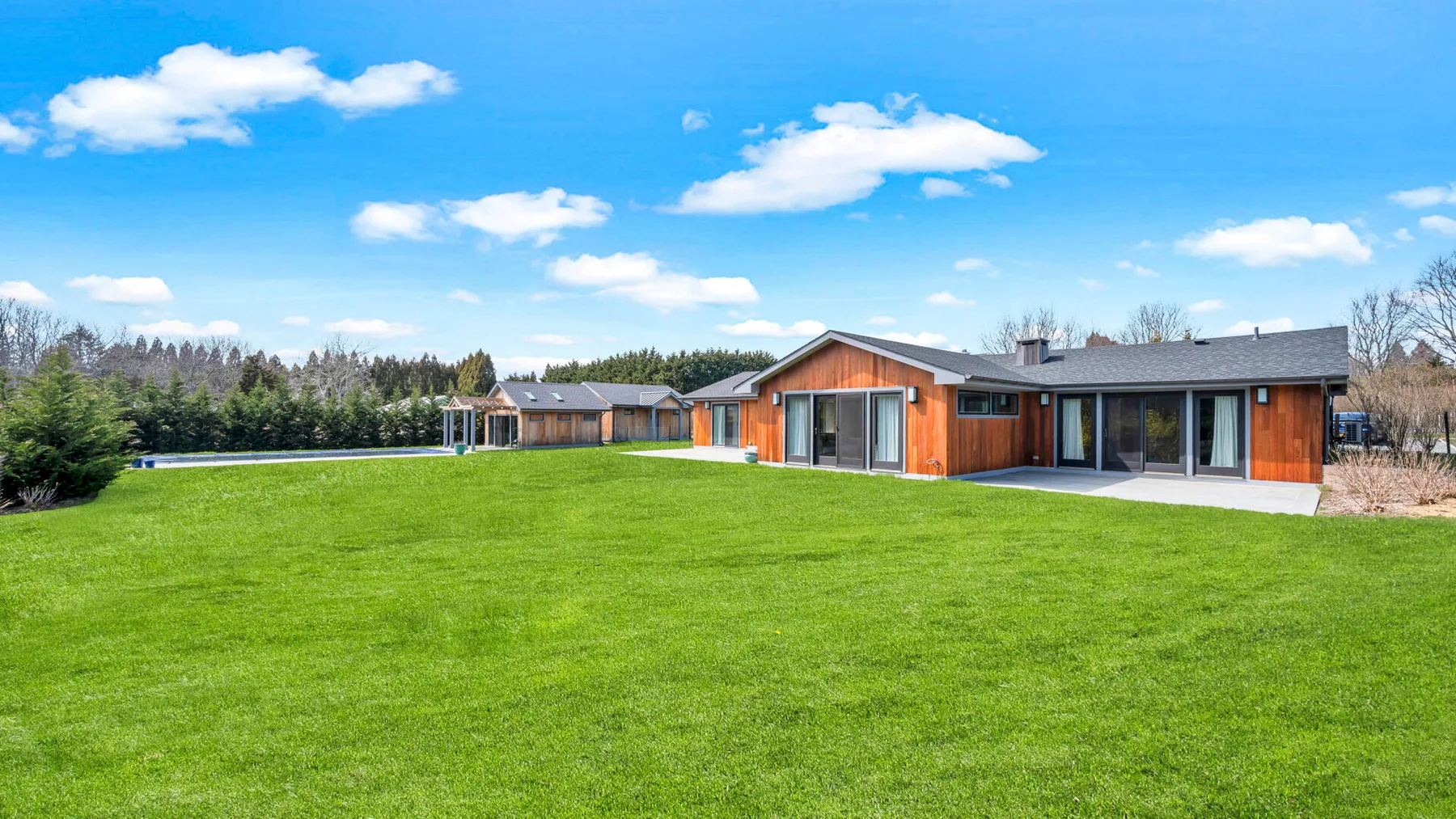 A modern house stands beyond a broad green lawn under a blue sky.