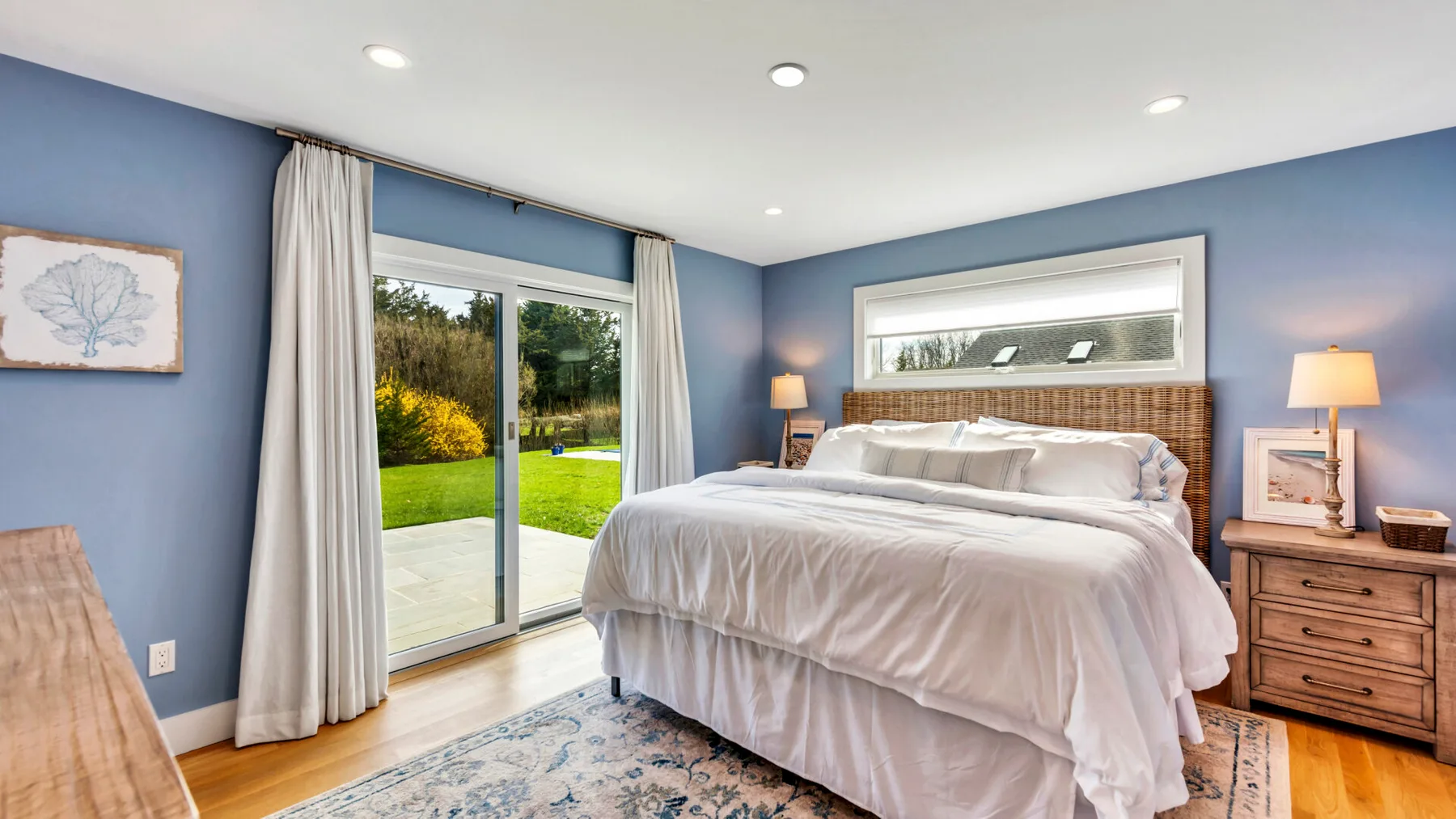 A bedroom with a large bed, blue walls, and sliding glass doors opening onto a garden.