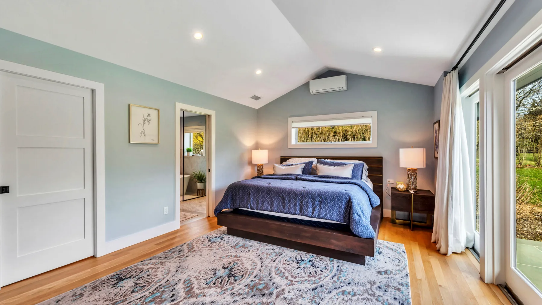 A bedroom with a bed, bedside tables, and large windows.