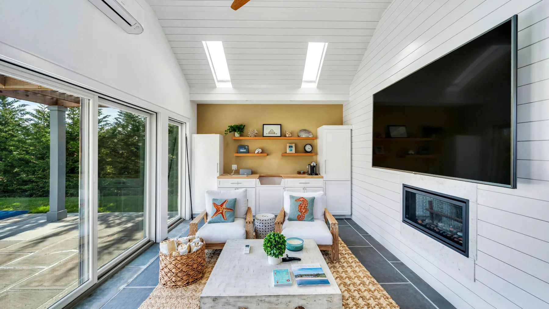 A bright sunroom with a low table, seating, and large windows overlooking greenery.