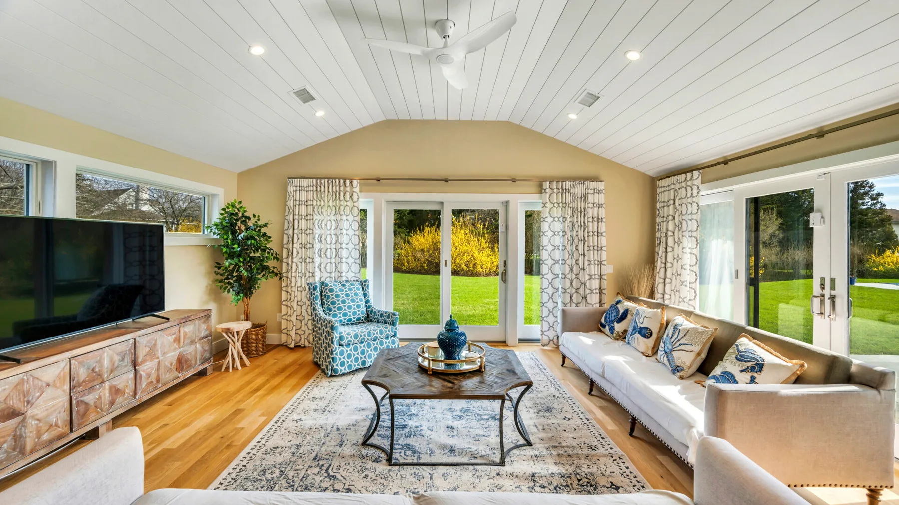 A bright living room has a sofa, a television, and glass doors opening to a garden.