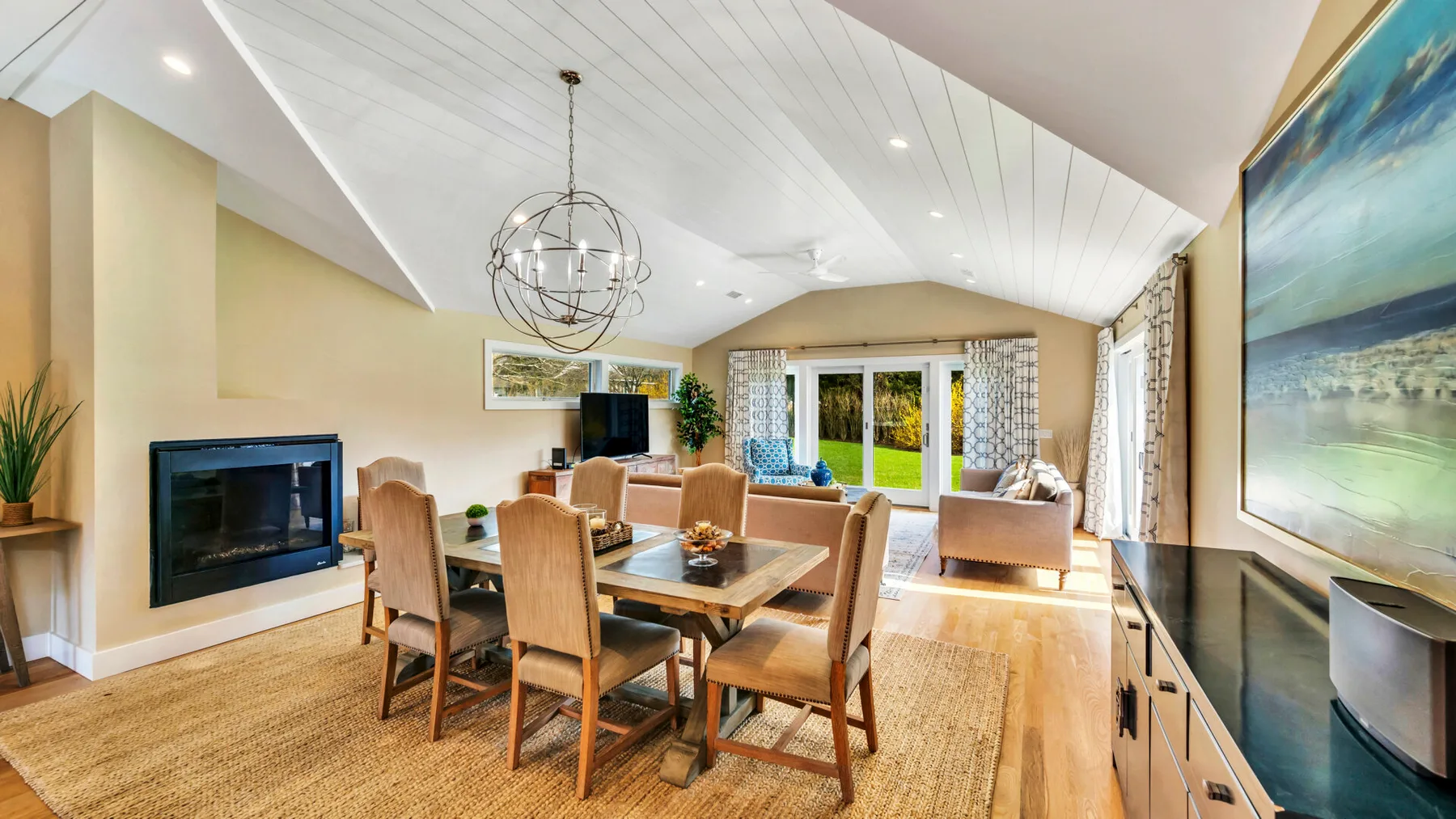 A bright living and dining area with a table, seating, and large windows.